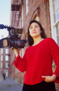 Julie Mallozzi with camera in front of brick building