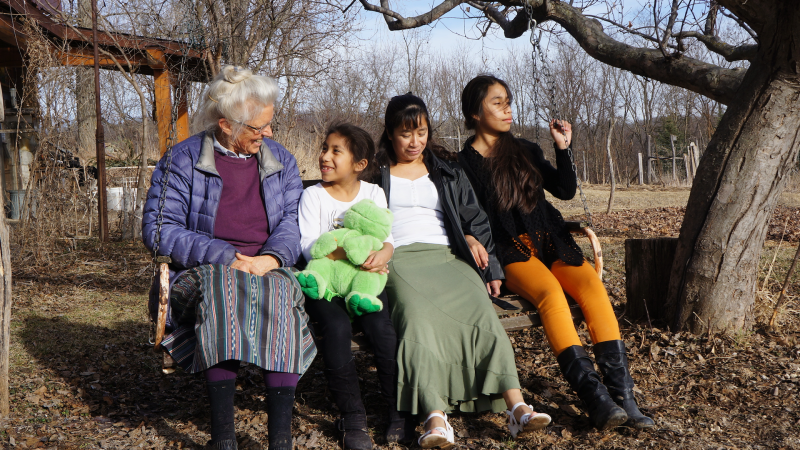 Four people sit on a swing - an elderly woman, and a mother and two kids.