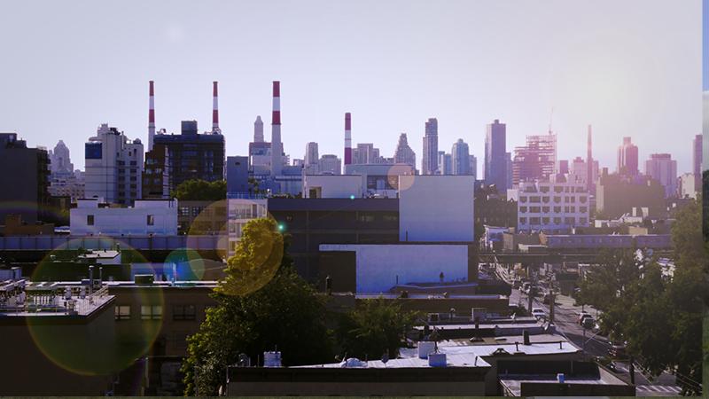 Wide angle shot of a city showing power plant chimneys and an elevated train line.