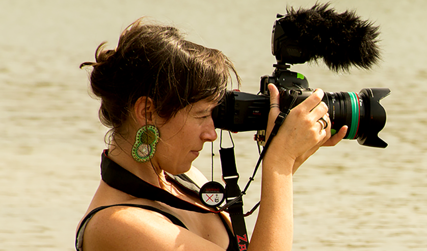 Side view shot of New Day Filmmaker Willow O’Feral, a white woman in her 30s, with dark hair and large earrings, who is looking into a camera.