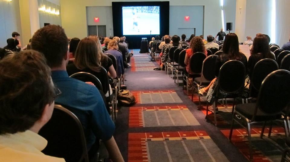 A nearly full presentation room at the conference. At the front, I’m Just Anneke is projected on a screen.