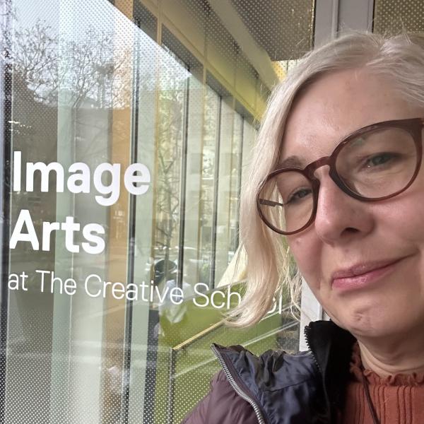 A woman with glasses standing in front of a glass that says "Image Arts at The Creative School"