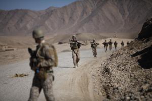 A column of armed American soldiers walks through barren, mountainous Afghanistan landscape