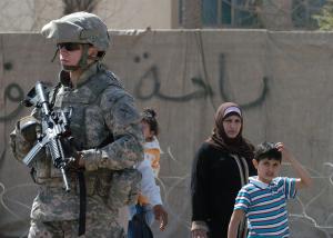 American soldier in full combat gear walks past Iraqi woman and child