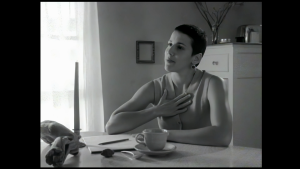 Terrylene, a woman with short dark hair, sits at a table with a note pad. One hand is on her heart.