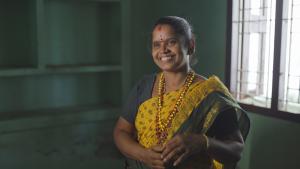 An Indian woman in a vibrant yellow and green sari, smiling radiantly.