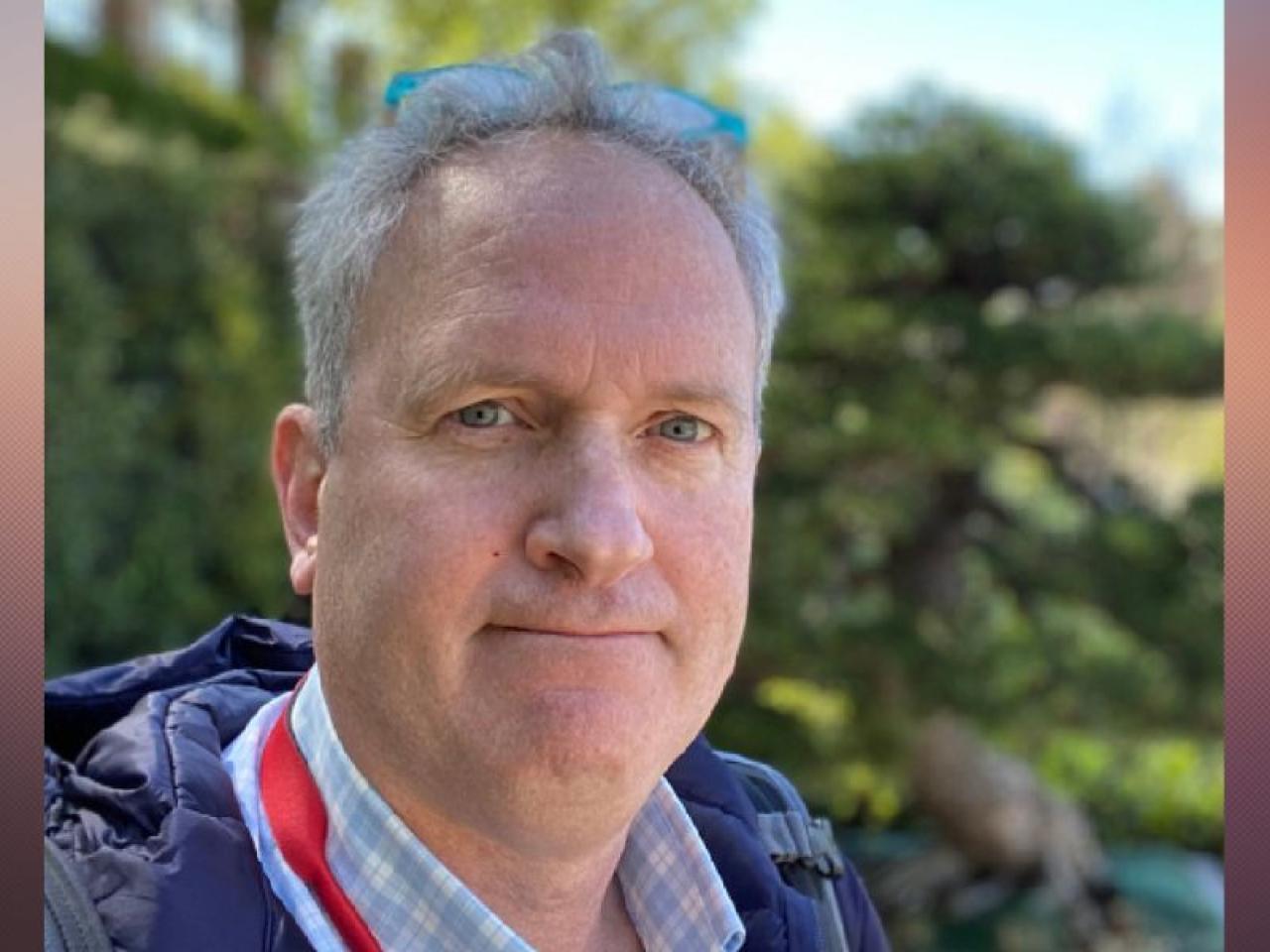 Portrait of a Caucasian man with short gray hair with glasses on top of his head outdoors